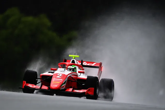 A red Formula 3 car emerging through spray at Spielberg